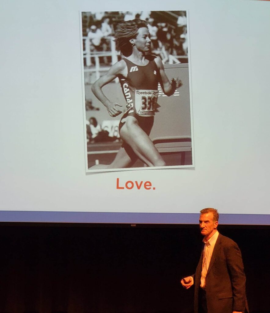 Jason Dorland speaking onstage beneath a presentation slide about love